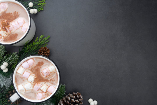 Hot chocolate mugs with marshmallows. Flat lay with fir branches. Gray background. Warm winter drink.
