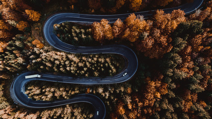 Aerial drone view of winding forest road in the middle of mountains. Colourful landscape with rural road, trees with yellow leaves.