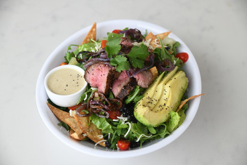 Steak and avocado over salad served in bowl