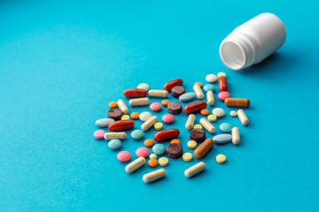 A handful of colored pills spilled out of the can on a blue background. Medical concept