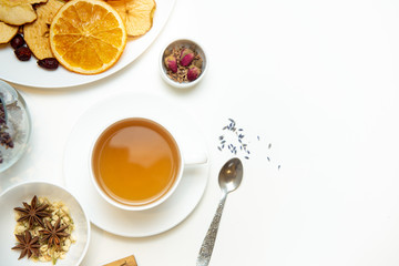a white mug on a white table with herbal tea and herbal ingredients laid out on the table. Concept on the topic of herbal treatment for colds and flu in autumn