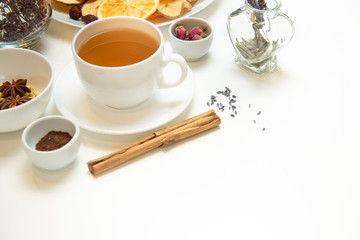 a white mug on a white table with herbal tea and herbal ingredients laid out on the table. Concept on the topic of herbal treatment for colds and flu in autumn