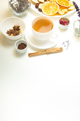 a white mug on a white table with herbal tea and herbal ingredients laid out on the table. Concept on the topic of herbal treatment for colds and flu in autumn