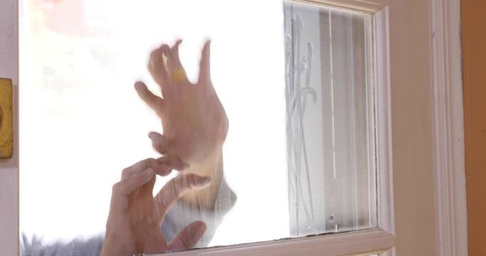 The hands of a dead zombie scrape at a window trying to get into a home.  	