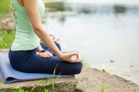 A young sports girl practices yoga on a green lawn by the river, yoga assans posture. Meditation and unity with nature