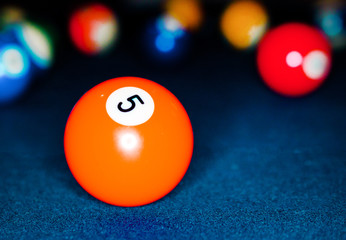 Macro closeup of Bright Orange 5 Ball with multicolored pool balls in the background on teal felted billiard table