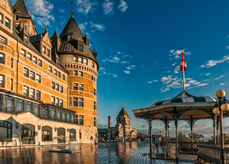 Fototapeta na wymiar A man runs on the Terrasse Dufferin outside the Chateau Frontenac on a early, wet autumn morning with a blue sky and clouds, with a green and white covered pavillion, railings and lightposts.