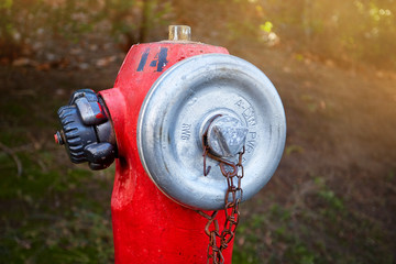 Old red fire hydrant with twisted lids on a background of plants
