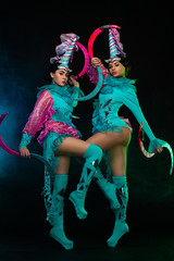 Two beautiful go-go dancer girls in freak costumes on disco party in color smoke. Night show women.