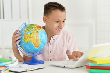Cute boy using laptop while holding globe