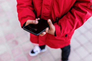 Unrecognizable kid boy using mobile in the street