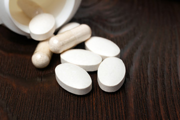 Fototapeta na wymiar White medical supplement pills and capsules on wooden background, macro image
