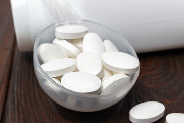 Fototapeta na wymiar White medical supplement pills in the plastic spoon on wooden background, macro image