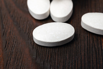 Fototapeta na wymiar White medical supplement pills on wooden background, macro image