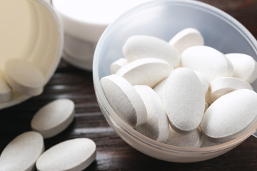 Fototapeta na wymiar White medical supplement pills in the plastic spoon on wooden background, macro image