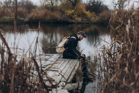 the guy is sitting lonely on the bridge and looking into the water against the backdrop of the lake