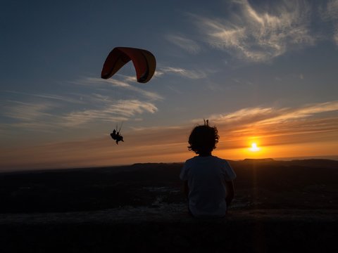 Child looking at flying tandem in evening sky.
