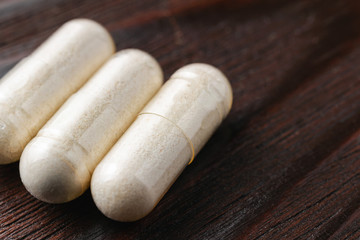 White medical capsules of glucosamine chondroitin, healthy supplement pills on wooden background, macro image