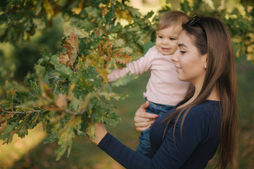 Portrait of beautiful family in the park. Mom and daughter togehter in autumn. Beautiful ten month baby on mother's hands