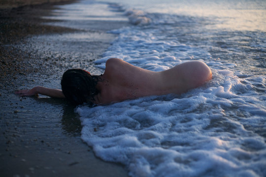 naked girl lies in the waves of the sea at sunrise on the shore