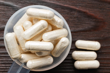 White medical capsules of glucosamine chondroitin, healthy supplement pills in the plastic spoon on wooden background, macro image, top view