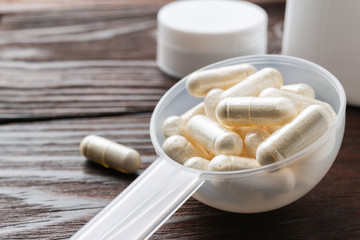 White medical capsules of glucosamine chondroitin, healthy supplement pills in the plastic spoon on wooden background, macro image