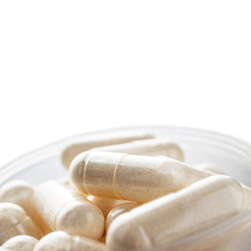 White medical capsules of glucosamine chondroitin, healthy supplement pills in the plastic spoon isolated on white background, macro image