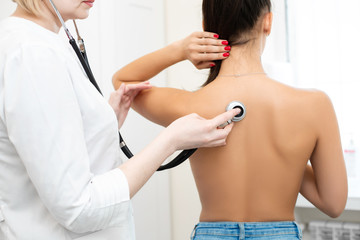 Doctor therapist examines a young girl, listens to her back with a stethoscope.