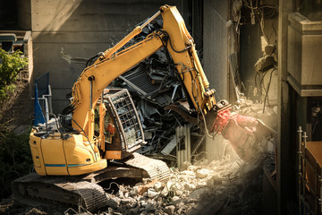 Heavy machinery surrounded with dust  cloud taking down an old building  - obrazy, fototapety, plakaty