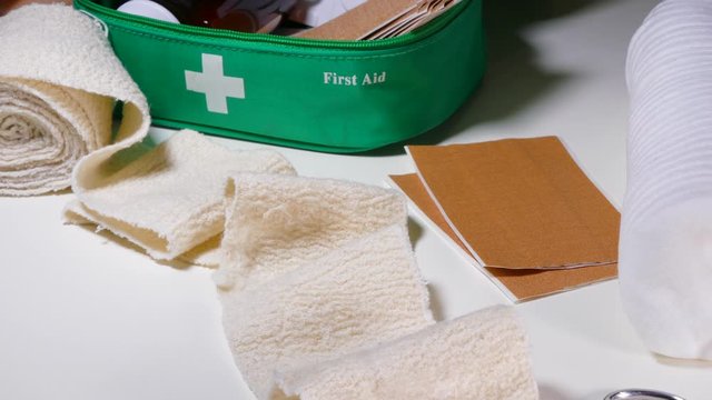 Close POV reverse dolly shot of a first aid kit, with sticking plasters, cotton wool, bandage and scissors, lying out of the bag on a table.