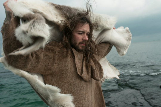 an atmospheric portrait of a man who wears the skin of an animal on the background of the waves of the sea