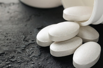Fototapeta na wymiar White medical supplement pills on dark background, macro image