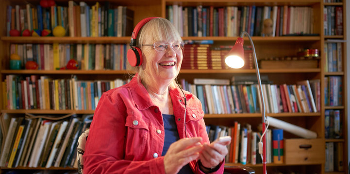 Happy woman in her 70s with headphones in cozy home library