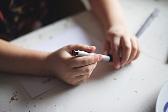 Close up of child's hand holding a pen procrastinating doing homework