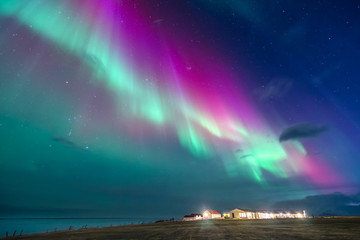 Naklejka premium kolorowe zorza polarna na islandzkiej plaży z domkami
