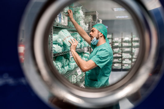 Male doctor in uniform and mask searching medical equipments on shelves