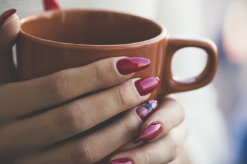 young girl with red manicure holding a orange cup of fragrant tea, autumn concept. Winter concept. Close up.