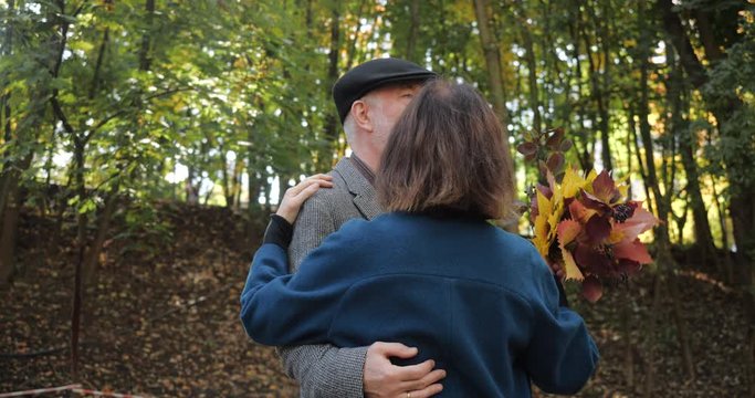 Happy elderly couple dancing on the alley of a beautiful park in the autumn - slow motion. Woman holds bouquet of leaves in her hands.