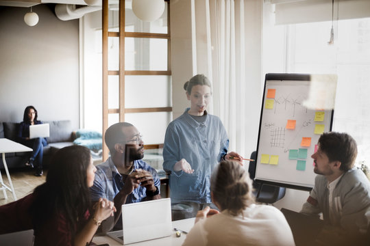 Businesswoman explaining business plan to colleagues in board room seen through glass wall