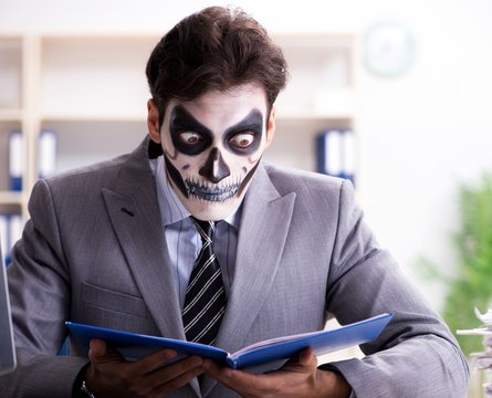 Businessmsn with scary face mask working in office