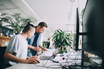 Male entrepreneurs discussing over document at desk in creative office