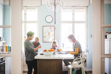 Father playing with son while standing by girl and woman busy at kitchen island