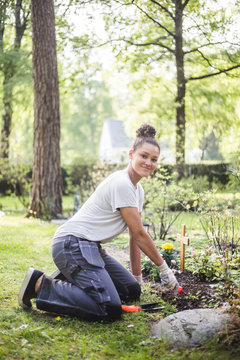 Full length portrait of young woman kneeling while planting at garden