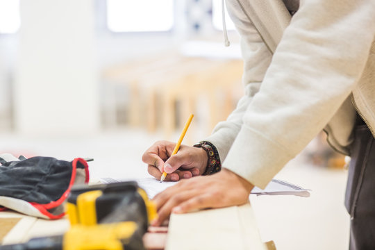 Midsection of male teenage carpenter drawing diagram on paper at workbench in workshop