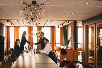 Colleagues shaking hands while lawyers working at table in board room