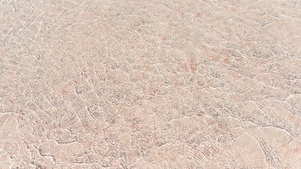 Beige texture. Clear water and pink sand. Water is with sun reflections. Background. Horizontal. Close-up