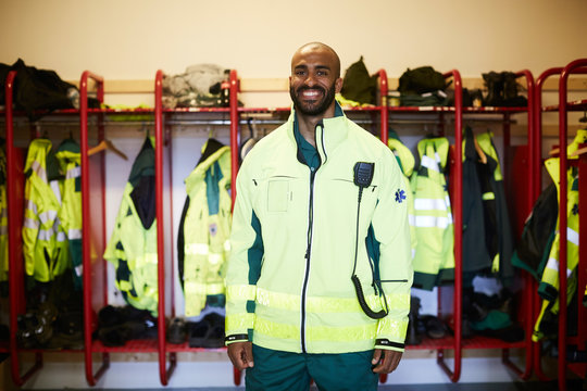 Portrait of smiling mid adult paramedic standing in locker room at hospital
