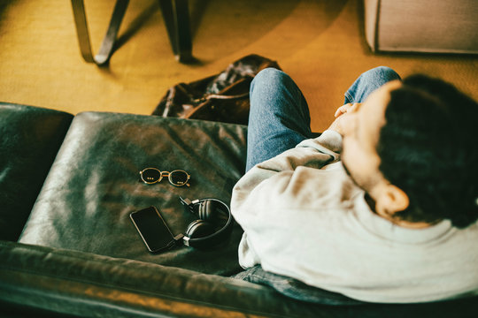 High angle view of man sitting by smart phone and accessories on sofa at hotel