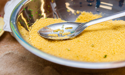 Macro Close Up View of Raw Couscous Grains and Parsley with a Steel Slotted Spoon in a Metal Bowl