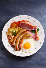 Full English or Irish breakfast with sausages, bacon, egg, tomatoes, fries and beans. Nutritious and healthy morning meal. View from above, top studio shot